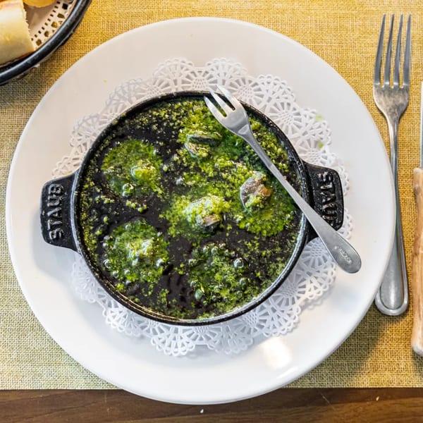 Escargots in garlic butter sauce, served in a black cast iron dish with a fork.