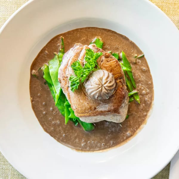 Seared tuna steak with green beans, topped with a dollop of sauce and parsley, in a brown sauce.