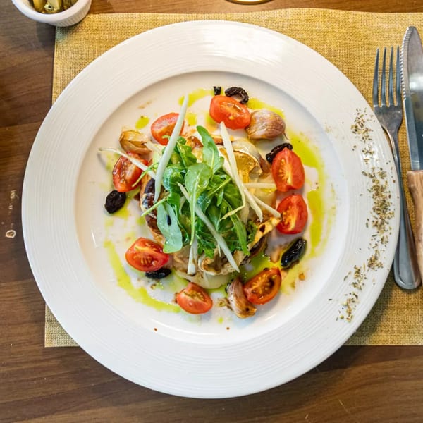 A gourmet dish with roasted vegetables, cherry tomatoes, olives, and arugula, drizzled with olive oil.