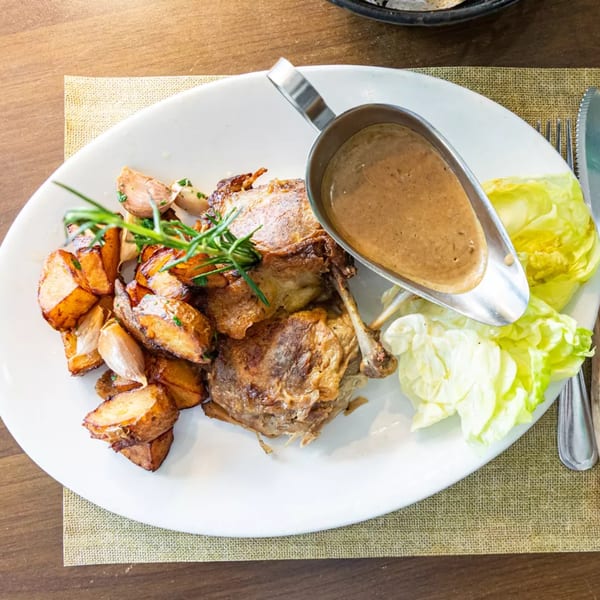 Roasted duck with potatoes, garlic, rosemary, and a side of lettuce and gravy.