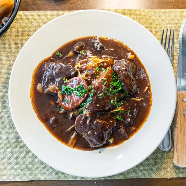 A white bowl filled with a rich, dark stew, garnished with fresh parsley, on a woven placemat.