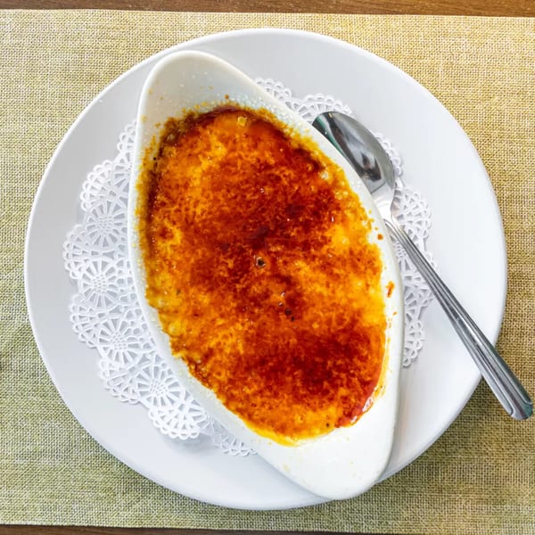 Crème brûlée in a white oval dish with a spoon on a white plate and placemat.