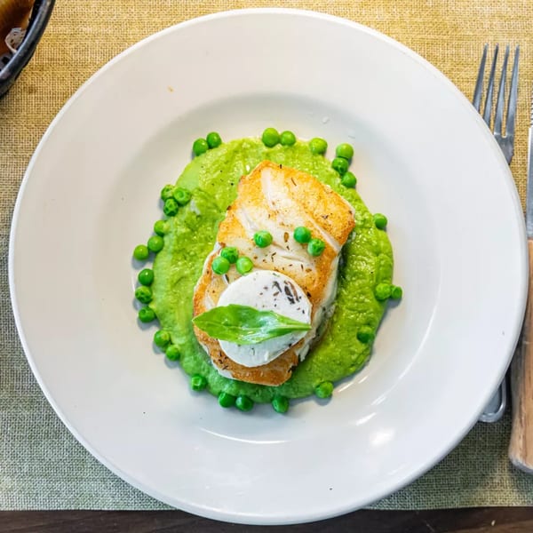 Pan-seared fish with a dollop of white sauce and a basil leaf, on a bed of pea puree.